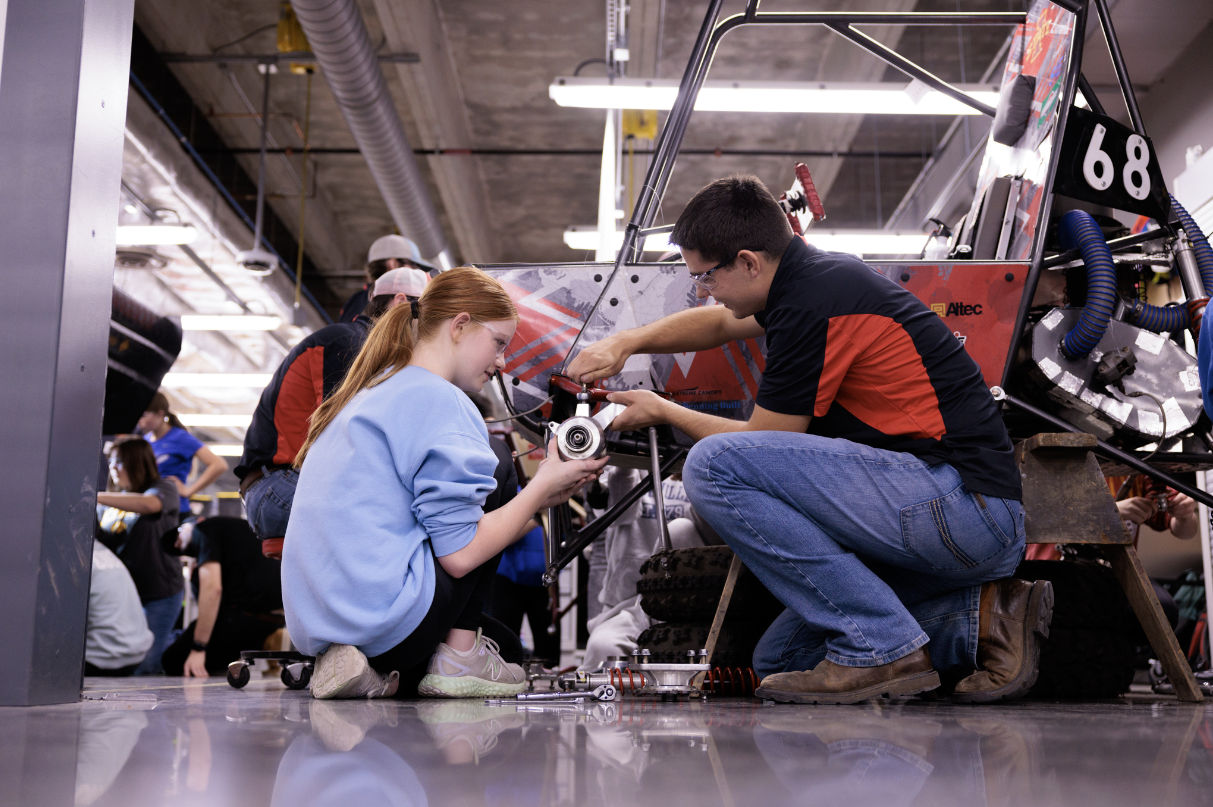 Iowa State student helping a conference attendee put a tire on a Baja vehicle